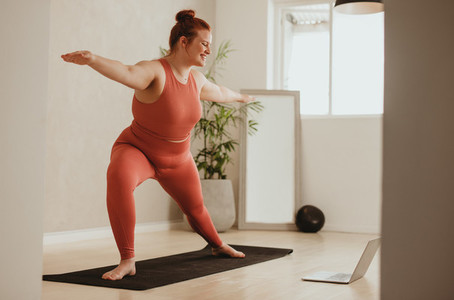 Woman exercising with watching workout class online on laptop