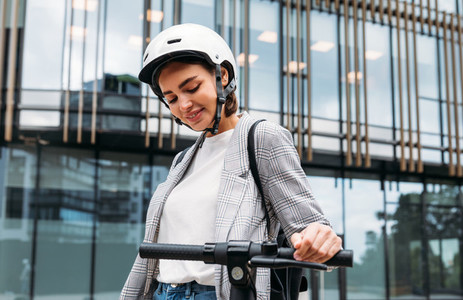 Young woman in helmet holding a handlebar of electric scooter in the city