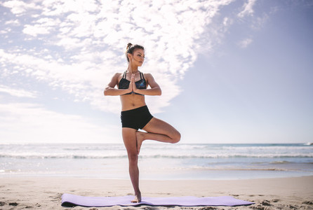 Woman at beach practicing yoga tree position