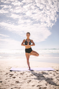 Fitness woman at beach meditating in tree pose yoga