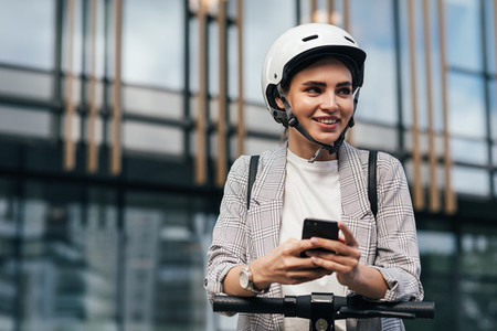 Cheerful woman in helmet using a mobile phone to unlock an electric scooter