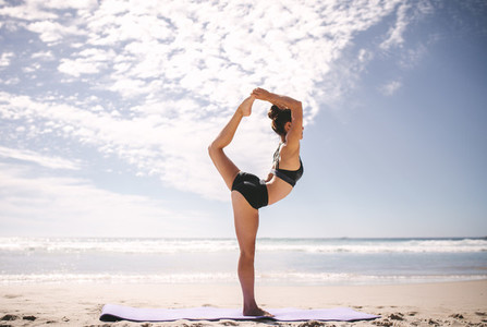 Woman doing Natarajasana yoga pose on the beach