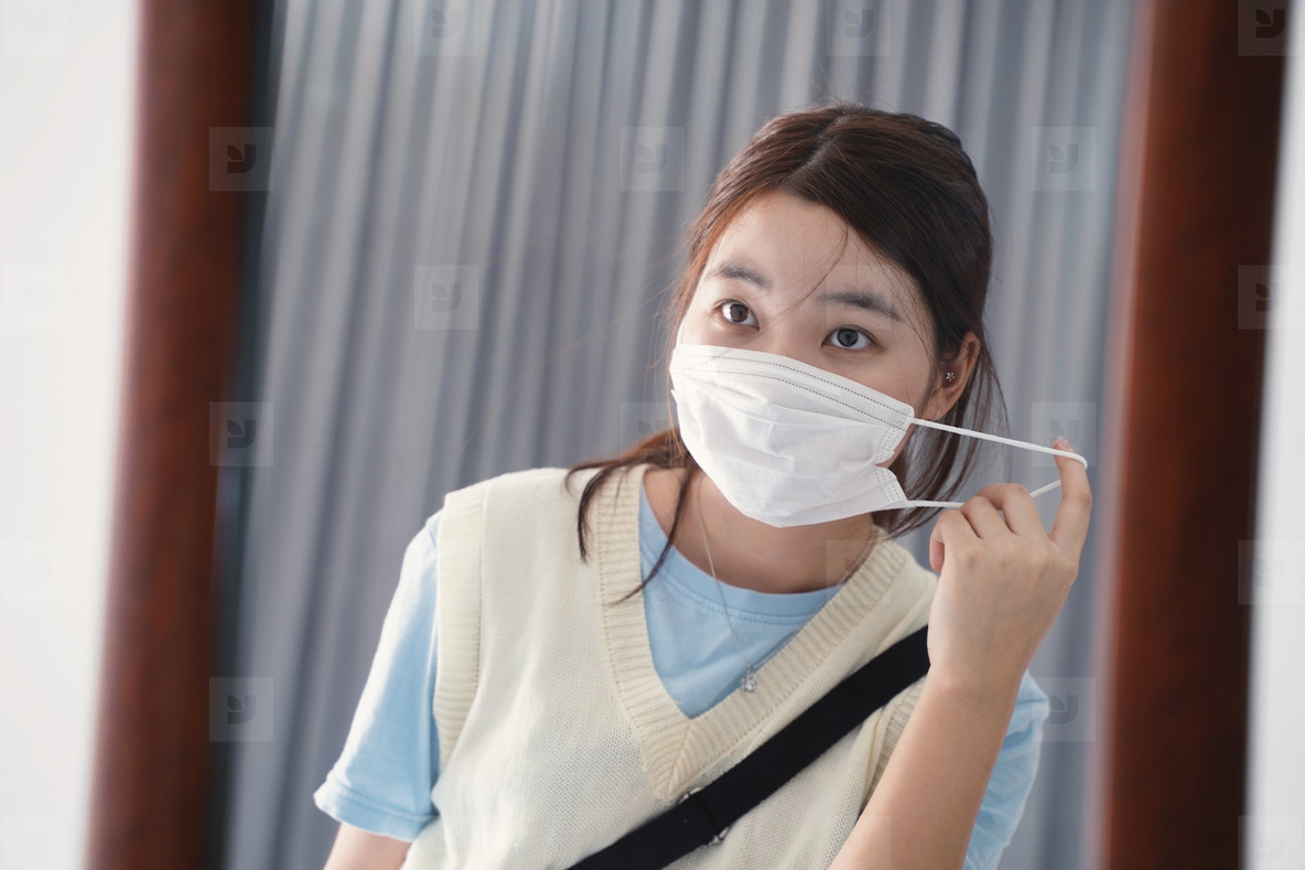 Young millennial asian woman wearing mask in front of mirror bef