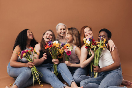 Group of multi ethnic women sitting together in studio Six smiling females with bouquets of flowers