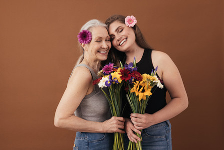 Two smiling women of different ages standing head to head in studio  Caucasian females with bouquets in hands and flowers in their hair