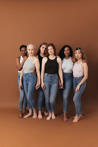 Studio shot of six women standing together holding their hands and looking at camera over brown background