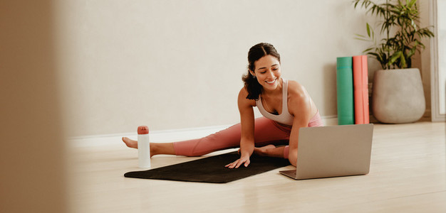 Woman stretching watching online training video on laptop