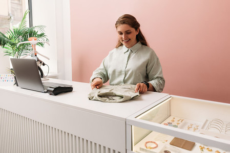 Saleswoman arranging clothes on a counter in store Clothing store owner working at a table