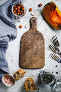 Empty wooden cutting board surrounded seasonal fall products Roasted pumpkin salad  kale  bread  nuts and seeds  Top view  food frame background