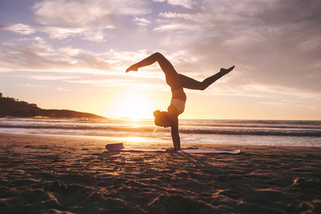 Woman doing yoga pose handstand on beach