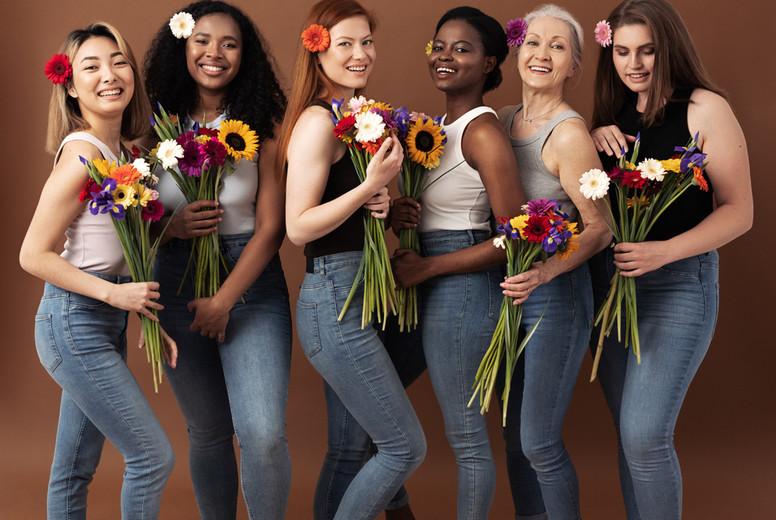 Full body shot of six women of different ages standing together with bouquets of flowers. Smiling women in casuals with flowers in hair.