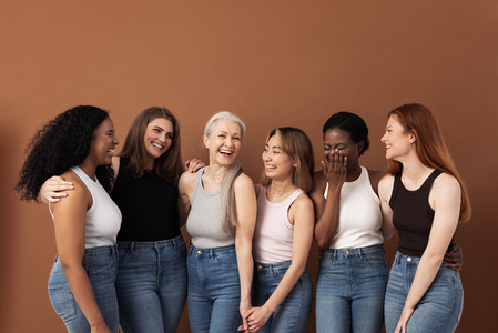 Stylish women of different ages having fun while wearing jeans and undershirts over brown background