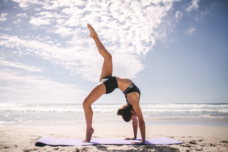 One legged wheel yoga pose on the beach