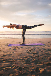 Warrior III yoga pose performed by fitness woman at beach