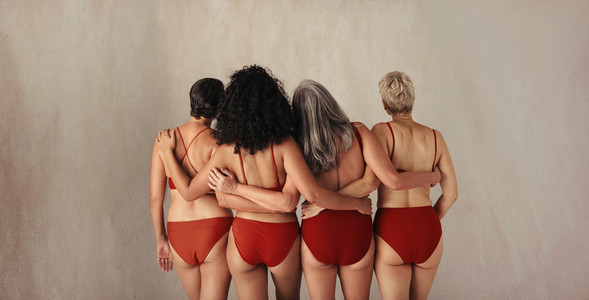 Rearview shot of four women of different ages embracing their na