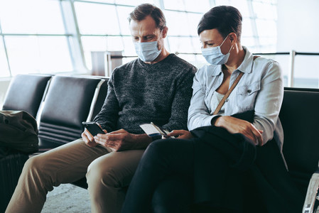 Man and woman in face masks using cell phone at airport terminal
