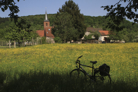 Bicycle parked in sunny idyllic meadow behind church Germany