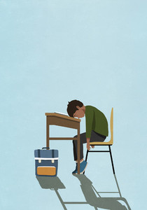 Exhausted schoolboy sleeping on classroom desk