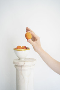Hand holding peach above bowl on pillar