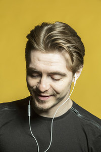 Portrait man listening to music with headphones on yellow background