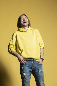 Happy man in jeans and hoody laughing against yellow background