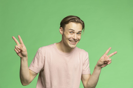 Portrait playful young man gesturing peace sign on green background