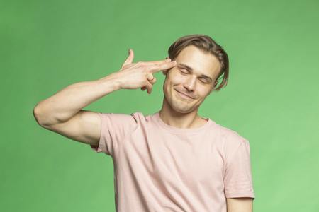 Portrait young man holding finger gun to head