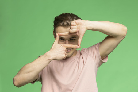Studio portrait young man gesturing finger frame on green background