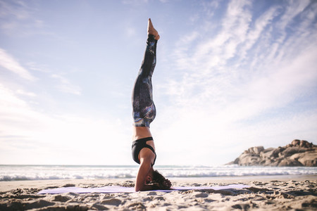 Woman in salamba sirsasana yoga pose at beach