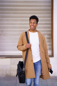 Young black man walking down the street carrying a briefcase and a smartphone in his hand