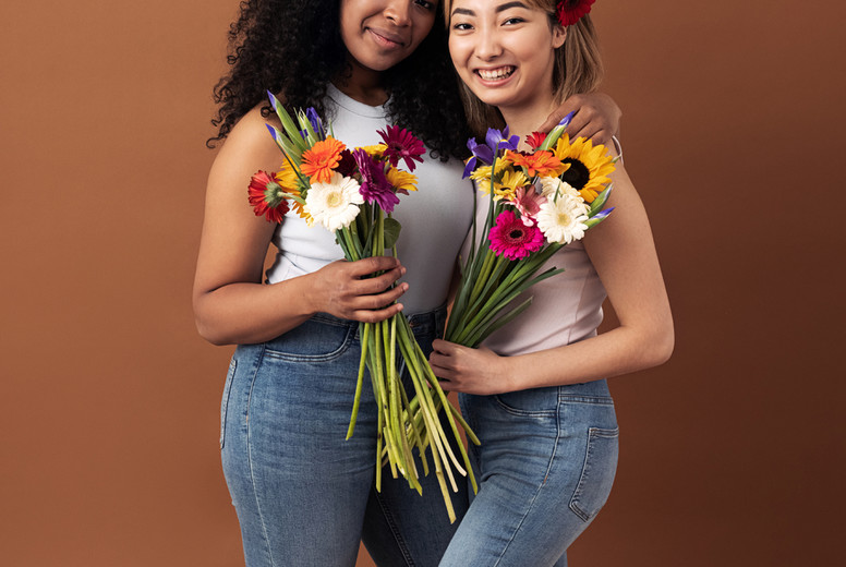 Asian and mixed race women posing against a brown background. Two smiling females with bouquets looking at camera