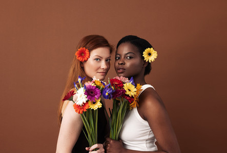 Two women of different races with flowers in their hairs holding bouquets  Caucasian and African American females looking at camera in a studio