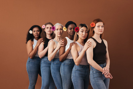 Six diverse female standing together over brown background  Women of different ages with flowers in their hair