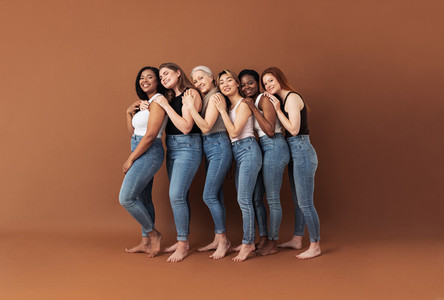 Full length of six smiling women embracing in studio  Females of different ages and body types posing over brown background