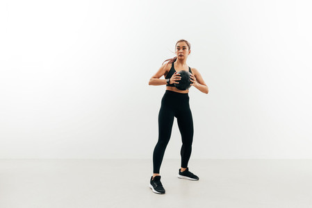 Full length of young sportswoman holding medicine ball against a white wall looking away