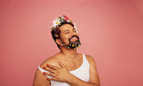 Smiling gay person wearing flowers on bed and beard