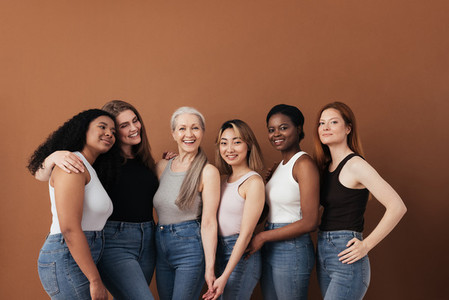 Multi ethnic group of women of different ages posing against brown background looking at camera