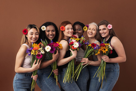 Six smiling women of different ages looking at camera in a studio  Happy diverse females with bouquets and flowers in their hairs standing together