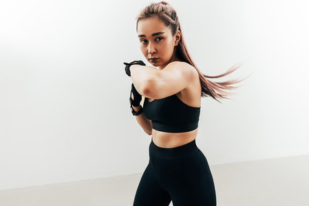 Woman doing kickboxing workout against a white wall  Female practicing punches