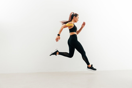 Runner in sport clothes sprinting near a white wall  Woman with kinesiology tape on shoulder jogging indoors