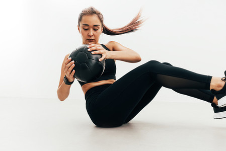 Woman doing abdomen exercises sitting indoors holding a medicine ball