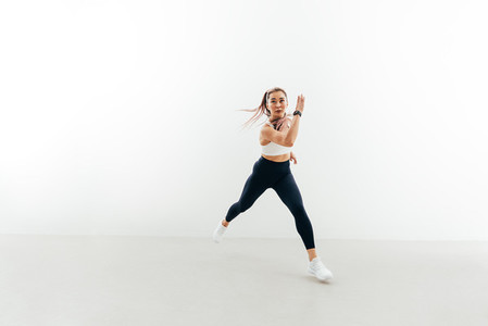 Young sportswoman running forward indoors  Muscular female exercising against a white wall