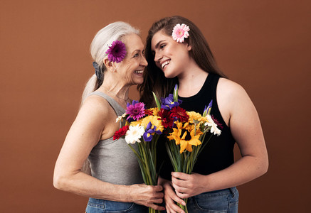 Two women of different ages with bouquets and flowers in their hair looking at each other