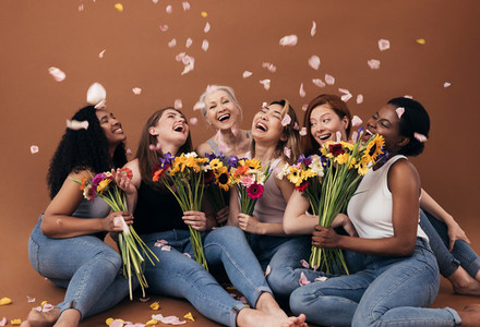 Group of diverse women with bouquets having fun under falling petals  Six happy females sitting together against a brown background