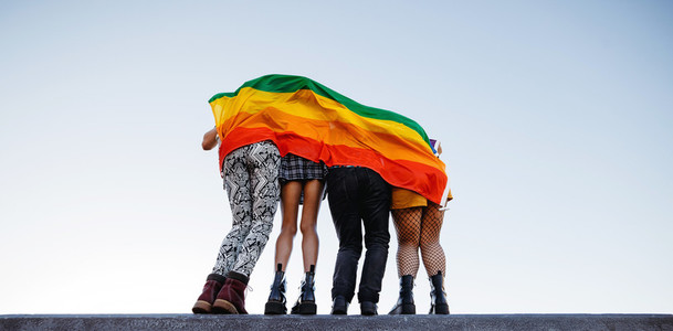 Anonymous group of people standing behind a rainbow flag