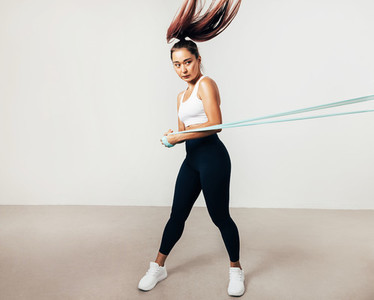 Muscular female athlete exercising with resistance band indoors