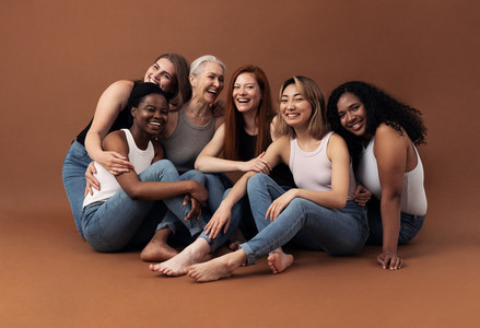 Portrait of six laughing women of different ages and body types sitting together on a brown background in studio