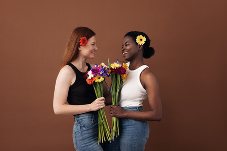 Two women of different races holding bouquets of flowers looking at each other in a studio