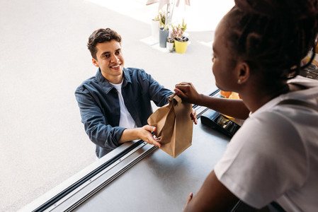 Young smiling man receiving a meal from a saleswoman  Male buying takeaway food