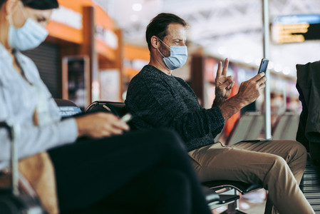 Man in face mask at airport terminal doing video call